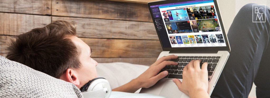 a man laying down in bed using his laptop to access twitch tv
