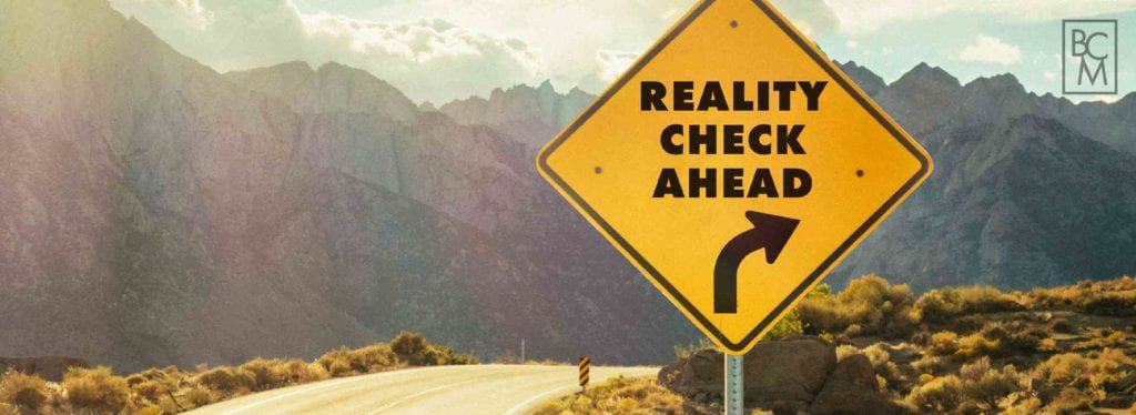 sign saying “reality check ahead” with mountains in background